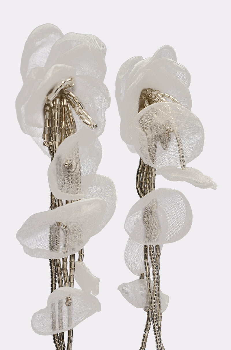 The IN YOUR DREAMS EARRING features two sheer drop earrings shaped like delicate white flowers with translucent fabric petals and metallic bead stems, displayed against a plain light background. 3