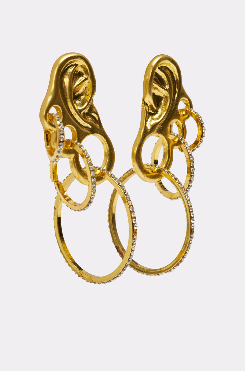 The IN MY EAR EARRING features gold ear-shaped designs with interlocking gold and rhinestone hoops, each crafted to resemble a human ear and displayed on a plain white background. 2