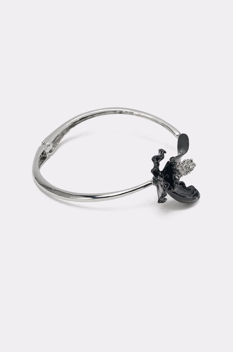 The FULL BLOOM NECKLACE is a silver-tone collar piece with an abstract black enamel pendant and a cluster of clear crystals on one side, shown against a plain white background. 2