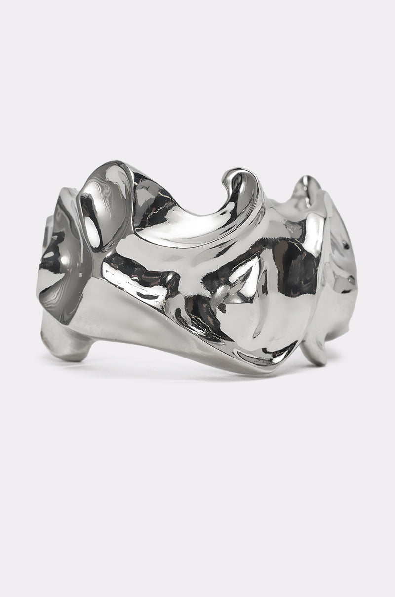 The MOLTEN DREAMS BRACELET is a wide, polished silver cuff with a sculptural wavy design and highly reflective surface—ideal for minimalist jewelry fans. Shown against a plain light background. 0