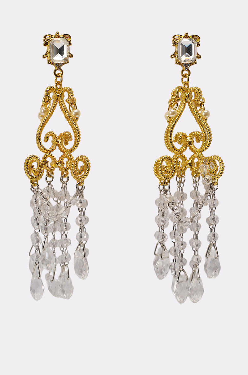 The SEE MY LIGHT EARRING features gold chandelier earrings with ornate filigree, a square gem top, pearl accents, and multiple crystal fringe dangles for a striking statement look. 0