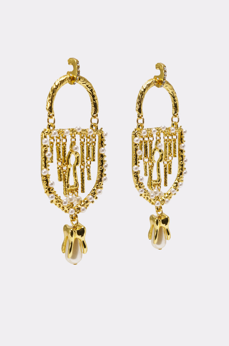 The UNLOCK ME EARRING is a pair of ornate gold statement earrings with intricate designs, baroque faux pearls outlining the arches, and a pearl-shaped charm dangling at the bottom, shown on a plain white background. 2