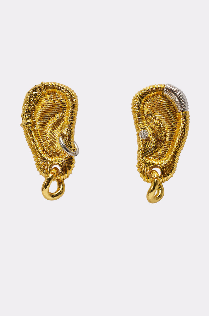 The HEARD U EARRING set features two sculptural gold statement earrings shaped like human ears with textured details, small silver accents, and one earring adorned with a small embedded gem. Shown on a plain white background. 2