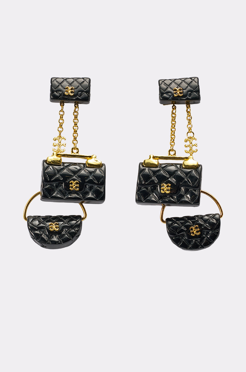 The GET ME A BAG EARRING features two mismatched statement earrings, each with three miniature black quilted purses adorned with gold chains and hardware, linked vertically by gold elements and shown on a plain white background. 0