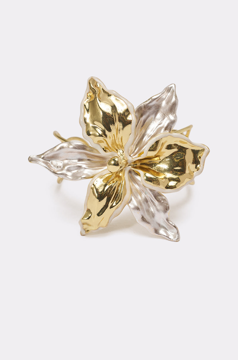 The BY THE SHORE BRACELET, a metallic flower-shaped accessory with five petals in gold and silver tones, showcases sculptural elegance and is displayed against a plain light background. 1