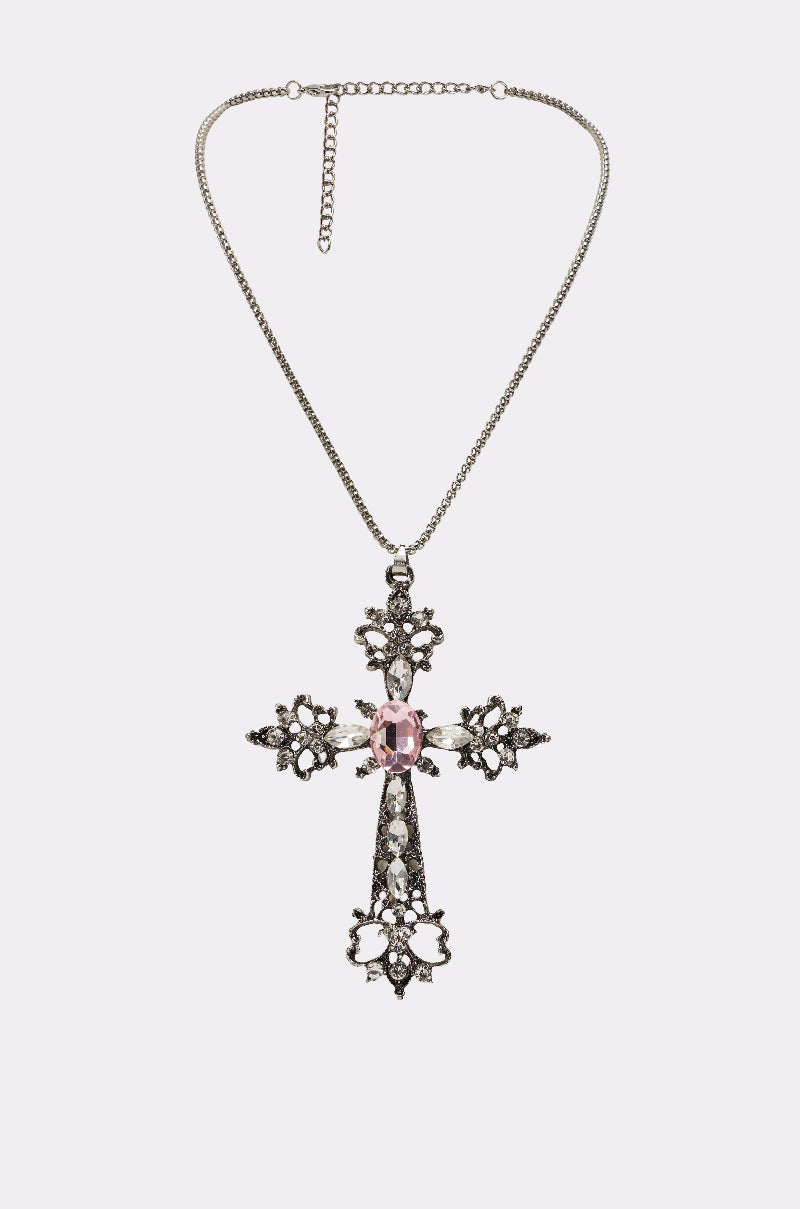 The LEXI NECKLACE is a gothic-chic piece featuring a silver chain, ornate rhinestone cross pendant with intricate floral designs, and a central pink gemstone accented by sparkling clear stones. 1