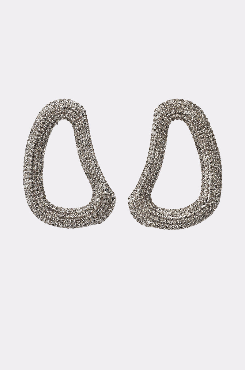 The GALA EARRING is a pair of silver-tone abstract earrings featuring an irregular hoop shape and a textured, sparkling surface, shown on a plain white background. 0