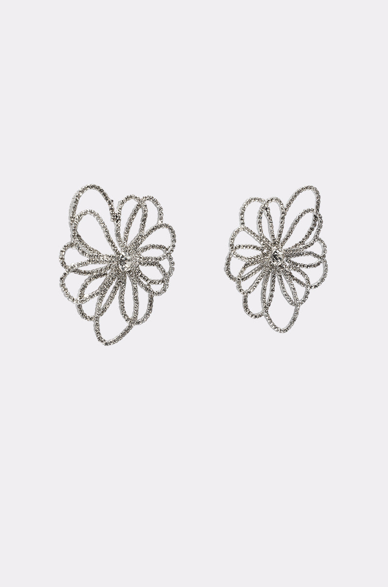 IM OUTSIDE EARRING: A pair of silver statement earrings shaped like abstract flowers with intricate looping petals, these crystal flower earrings gleam against a plain white background. 3