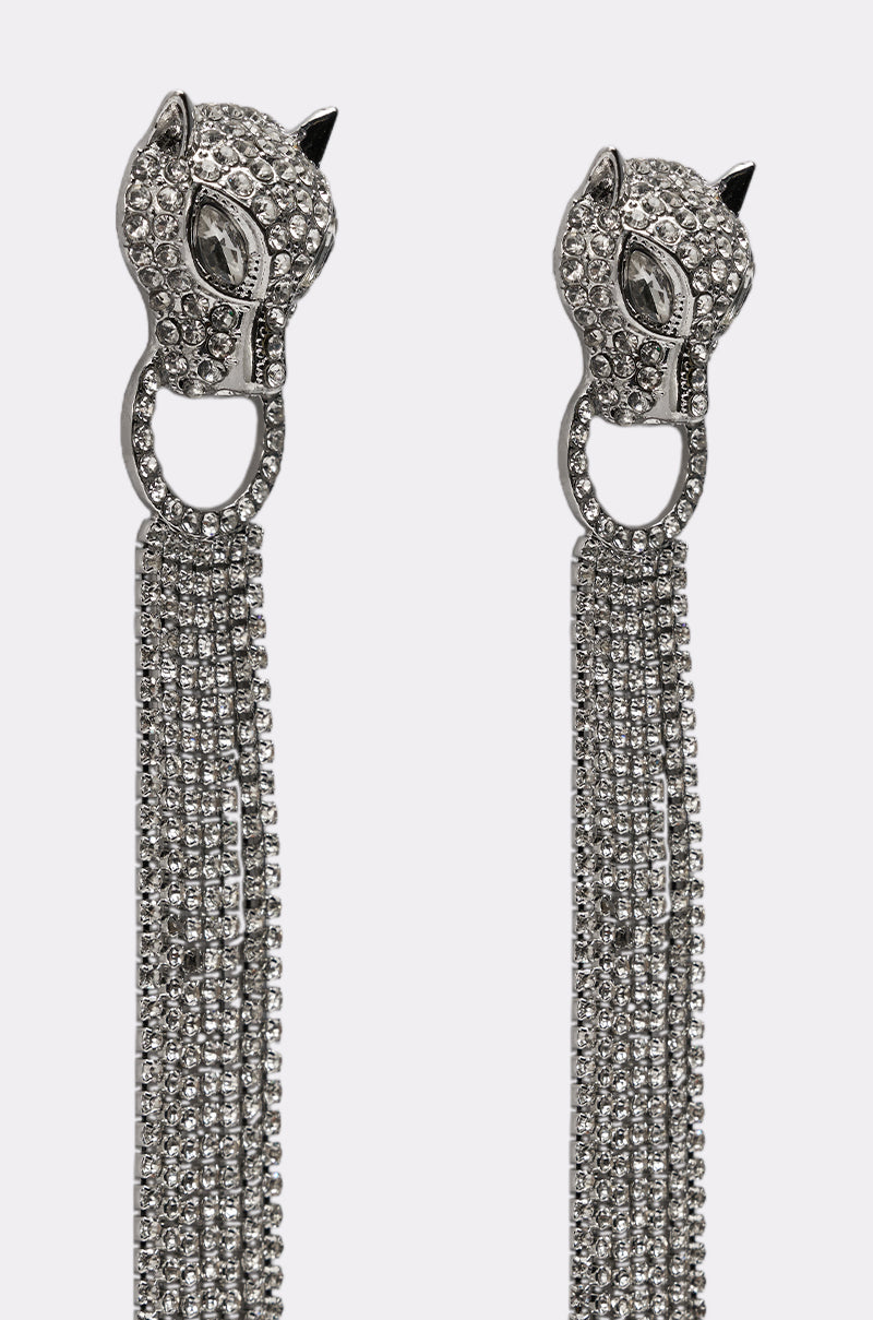 The AT THE GALA EARRING is a pair of silver, rhinestone-encrusted statement earrings with animal head designs and pointed ears, featuring long, sparkling chain dangles. 3