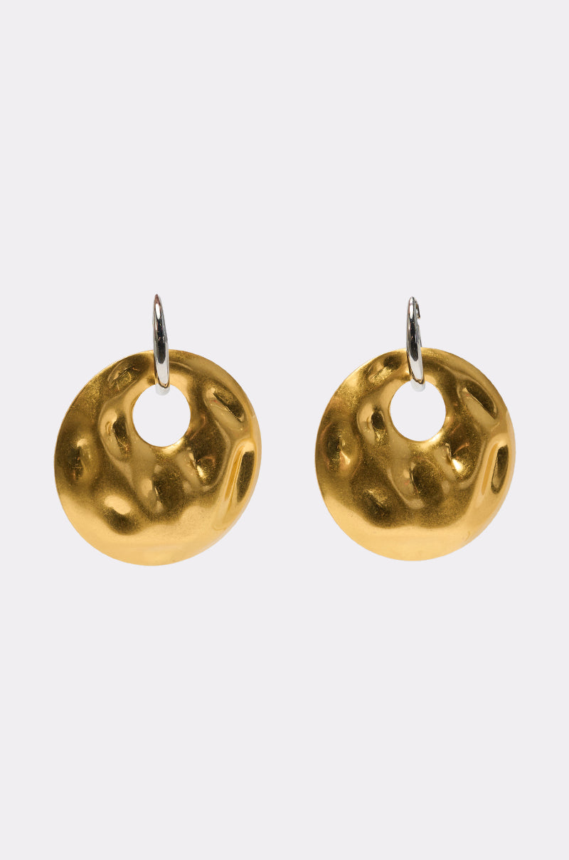 LEMME IN EARRING: Round, gold-toned hammered disc earrings with irregular dimpled surfaces and silver hooks, displayed on a plain light background. 0