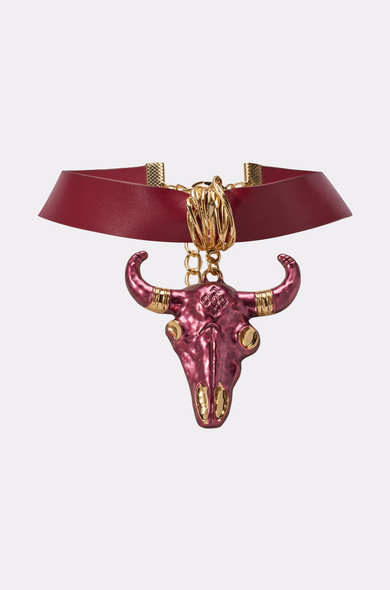 The RED HOT NECKLACE is a western-inspired red faux leather choker with a large metallic magenta bull skull pendant with gold accents, suspended from gold rings. 0