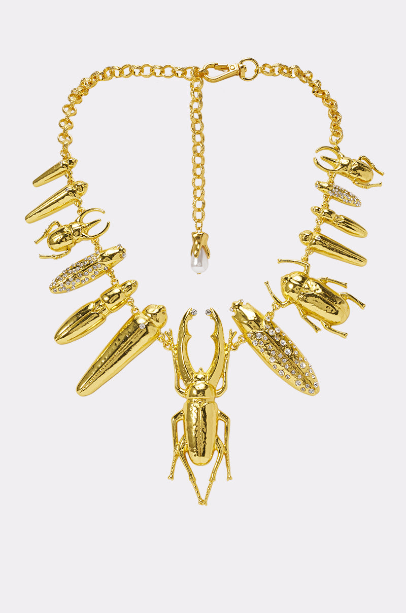 The QUIT BUGGIN NECKLACE is a gold statement piece featuring an array of beetle-shaped charms—some accented with sparkling crystals—artfully arranged along the chain and centered by a striking large beetle pendant, creating a truly stunning beetle charm necklace.