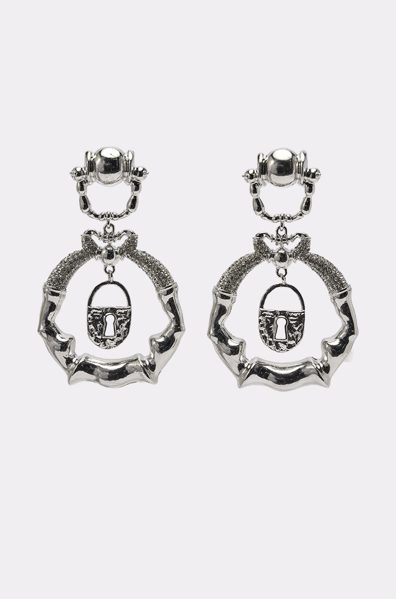 The FLEW OUT EARRING features silver statement drop earrings with textured, bone-inspired designs and a central hanging padlock charm, displayed against a plain white background. 1