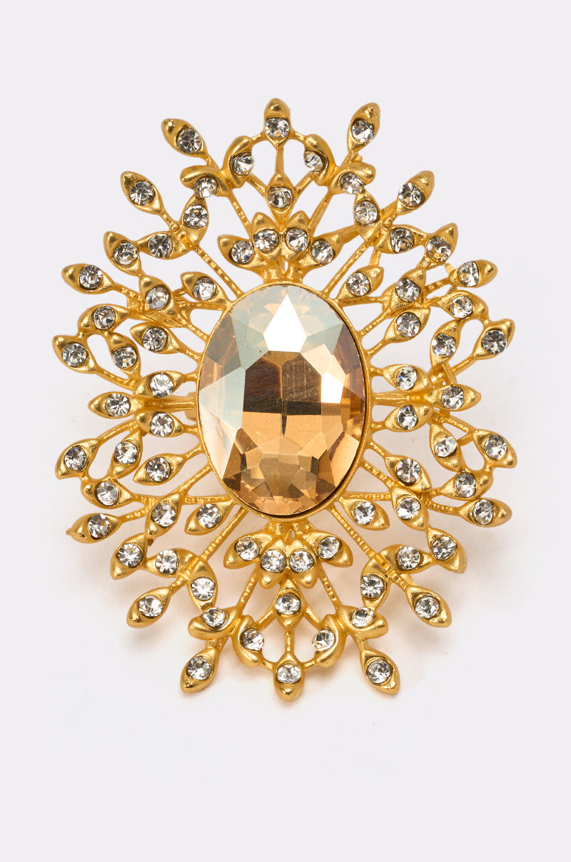 Pair the TAKE ME OUT RING with a gold brooch featuring an intricate floral design, an oval faceted amber gemstone at the center, and clear crystals for a striking statement look. 0