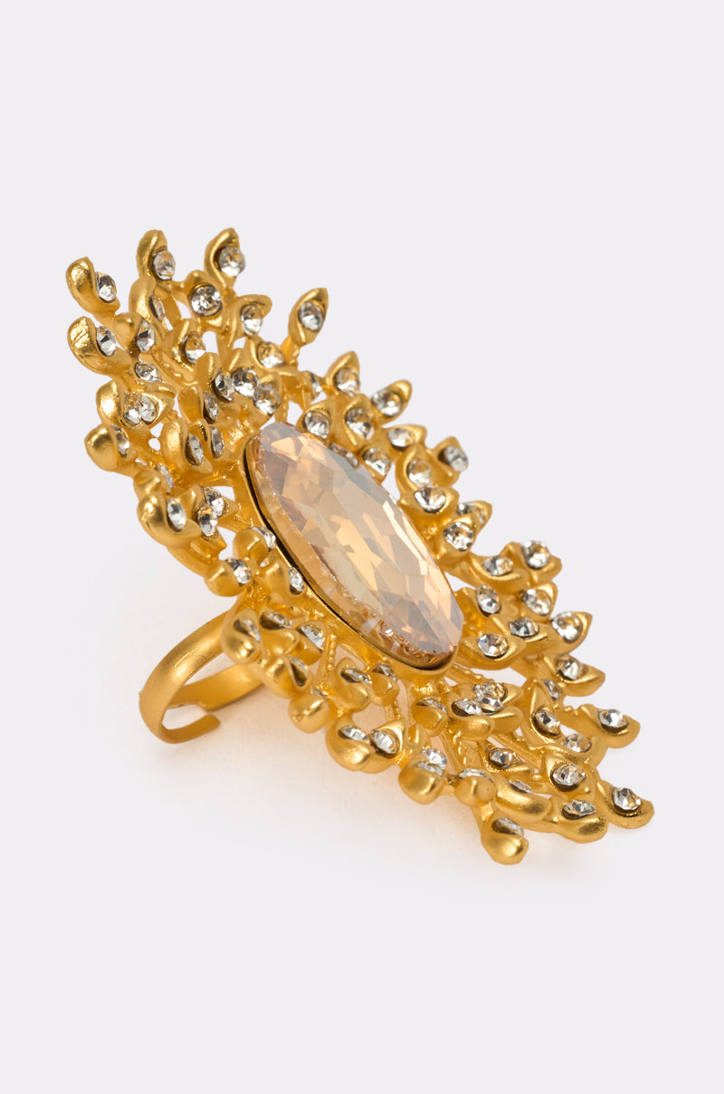 The TAKE ME OUT RING is a gold cocktail ring featuring an ornate, floral-inspired design with a large oval central gemstone encircled by smaller clear stones. 2