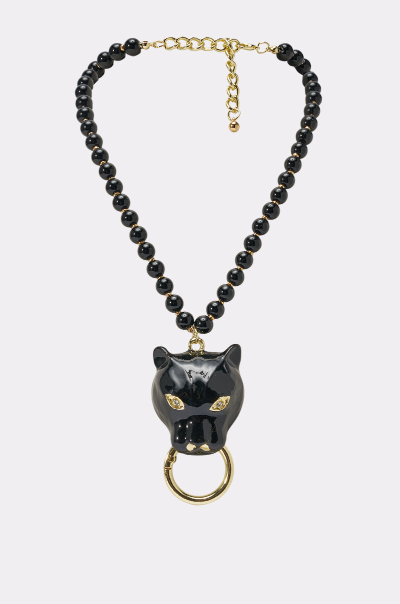 The TOO TUFF NECKLACE is a black beaded statement piece featuring glossy beads and a striking panther pendant with gold eyes and a gold ring, all on an adjustable gold chain—ideal for bold streetwear style.
