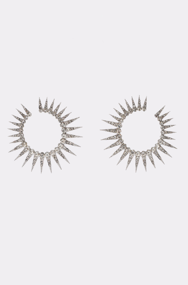 Introducing the STAR NIGHT EARRING—a dazzling pair of silver earrings with a radiant starburst design. Each earring features evenly spaced, spiked points that create a striking sunburst effect, while the textured surface is adorned with shimmering rhinestones for extra sparkle. These rhinestone earrings are the perfect choice to add a touch of brilliance to your evening jewelry collection.