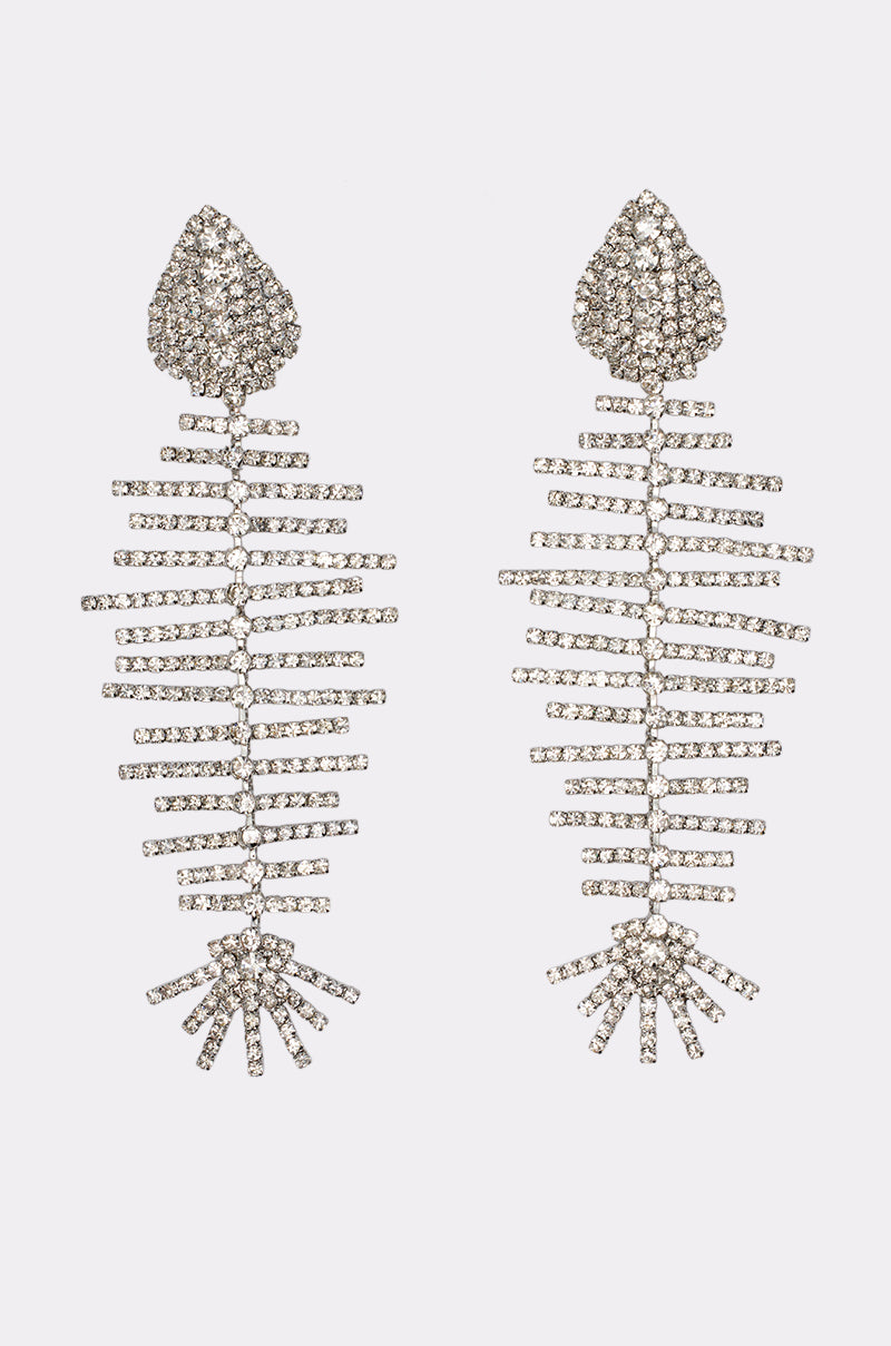A pair of GLOW MODE BEDAZZLED EARRINGS, intricately crafted from sparkling silver rhinestones in an oversized fishbone design, dangle elegantly against a plain white background.