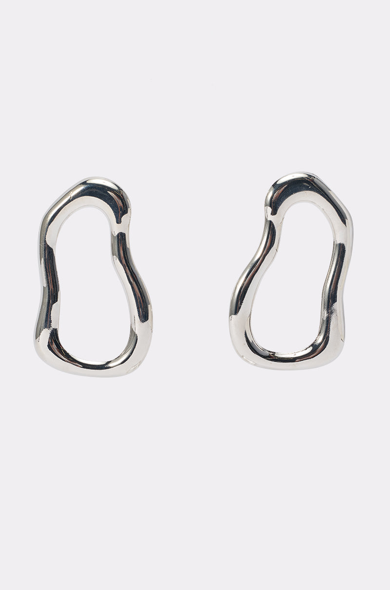A pair of WAVEY BABY DANGLE EARRINGS IN SILVER featuring an abstract, irregular wavy shape and a smooth, shiny finish, displayed on a plain white background.