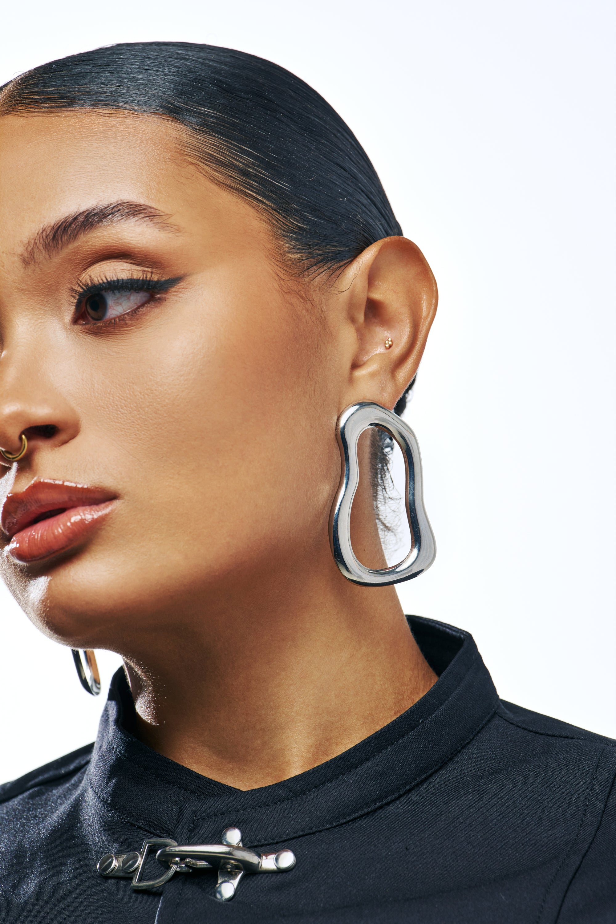 A person wearing a WAVEY BABY DANGLE EARRING IN SILVER, a large, wavy circular dangle earring.