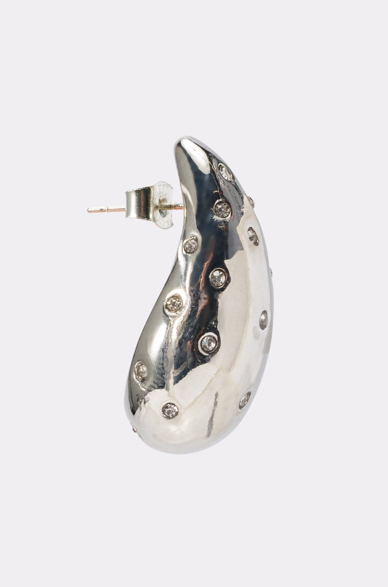 The ELLE EARRING is a single silver statement piece with smooth curves and shiny finish, accented by small gemstones. Ideal for nights out, it stands out beautifully against a plain, light-colored background. 2