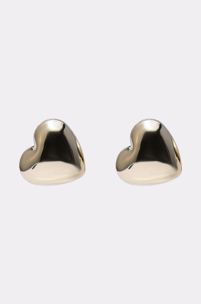 The PUFFY HEART EARRING is a pair of shiny, gold-colored, heart-shaped stud earrings displayed on a simple light background. 1
