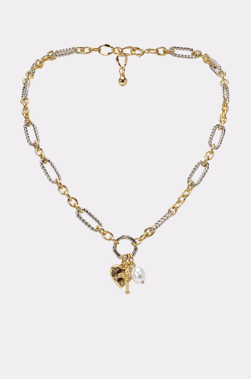 The CHARMED LIFE NECKLACE is a mixed-metal chain with textured gold and silver links, featuring a pearl accent, a heart charm, and a decorative toggle clasp at the center.