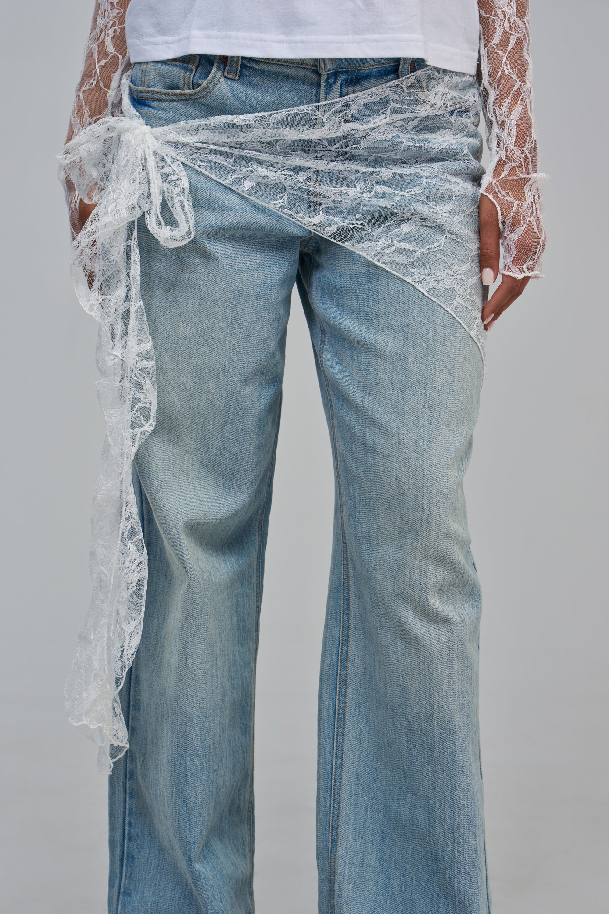 A person wearing light-wash denim jeans with a white sheer mesh lace ANGEL LACE SCARF tied at the waist and a matching long-sleeve top.