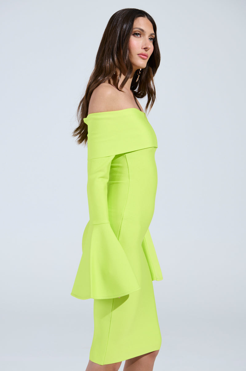 A woman poses in profile in the WORK OF ART BANDAGE MIDI DRESS IN LIME, featuring flared off-the-shoulder sleeves. The vibrant neon green midi dress complements her long dark hair and neutral expression against a plain, light background.