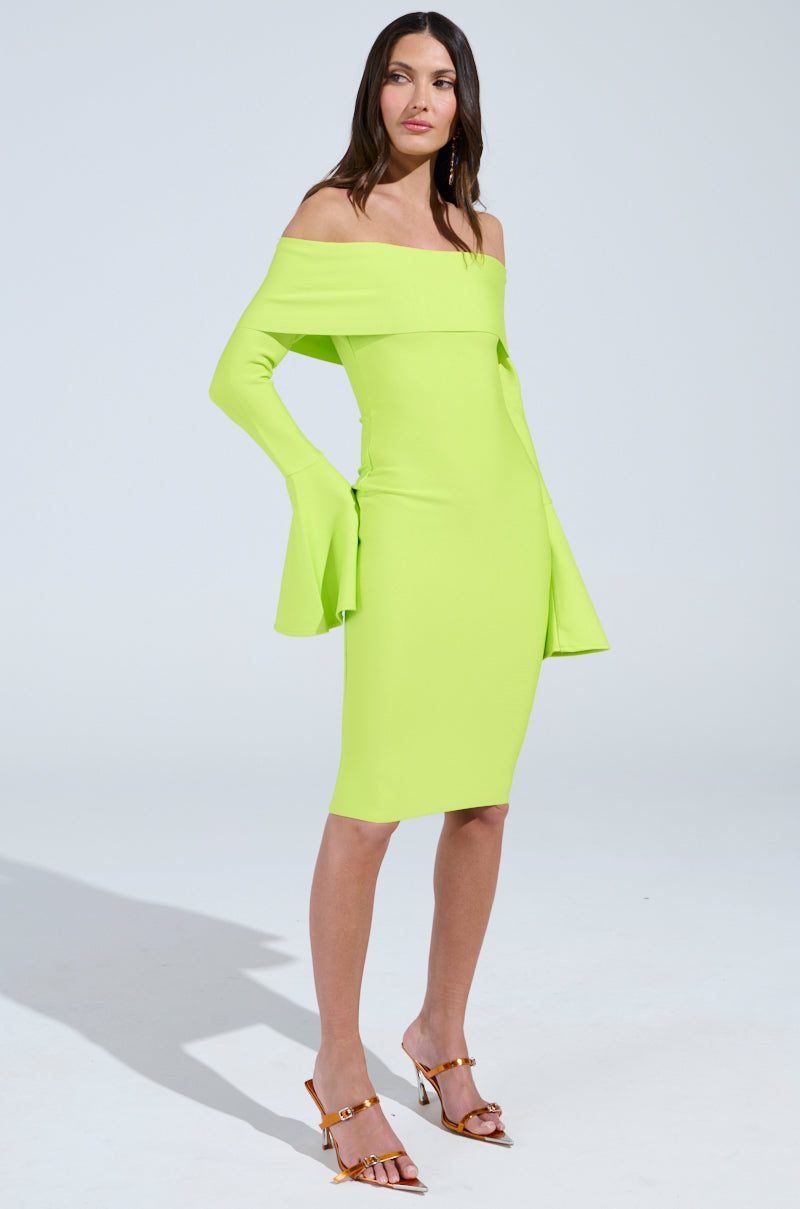 A woman models the "WORK OF ART BANDAGE MIDI DRESS IN LIME," an off-the-shoulder, long-sleeved bandage dress with flared cuffs that reaches knee-length. She pairs it with open-toed heels against a plain light gray background.