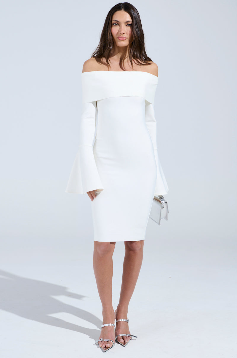 A woman dons the "Work of Art" white bandage midi dress, featuring off-the-shoulder and long bell sleeves. She accessorizes with a silver clutch, and strappy silver heels highlight the bodycon fit. The plain background enhances her elegant outfit.