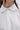 Close-up of a person wearing the KIND OF A BIG DEAL POPLIN HIGH LOW DRESS IN WHITE. Only the lower face, neck, and upper chest are visible. The dress features white buttons, and long dark hair is partially shown.