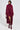 A person stands against a plain background, wearing a deep burgundy faux mohair knit sweater dress with the PINKY PROMISE SOFT KNIT CARDIGAN and glossy burgundy knee-high boots. They hold a small patterned purse and have short, sleek hair.