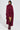 A person stands confidently in a coordinated burgundy outfit: a textured turtleneck dress, the PINKY PROMISE SOFT KNIT CARDIGAN for added warmth, and glossy knee-high boots. They hold a small patterned handbag, posing against a plain background.