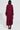 A person with short black hair is wearing the PINKY PROMISE SOFT KNIT CARDIGAN, along with long, fluffy burgundy coat that resembles faux mohair and dark burgundy knee-high boots. They're standing against a plain background, facing away, holding a small patterned clutch.