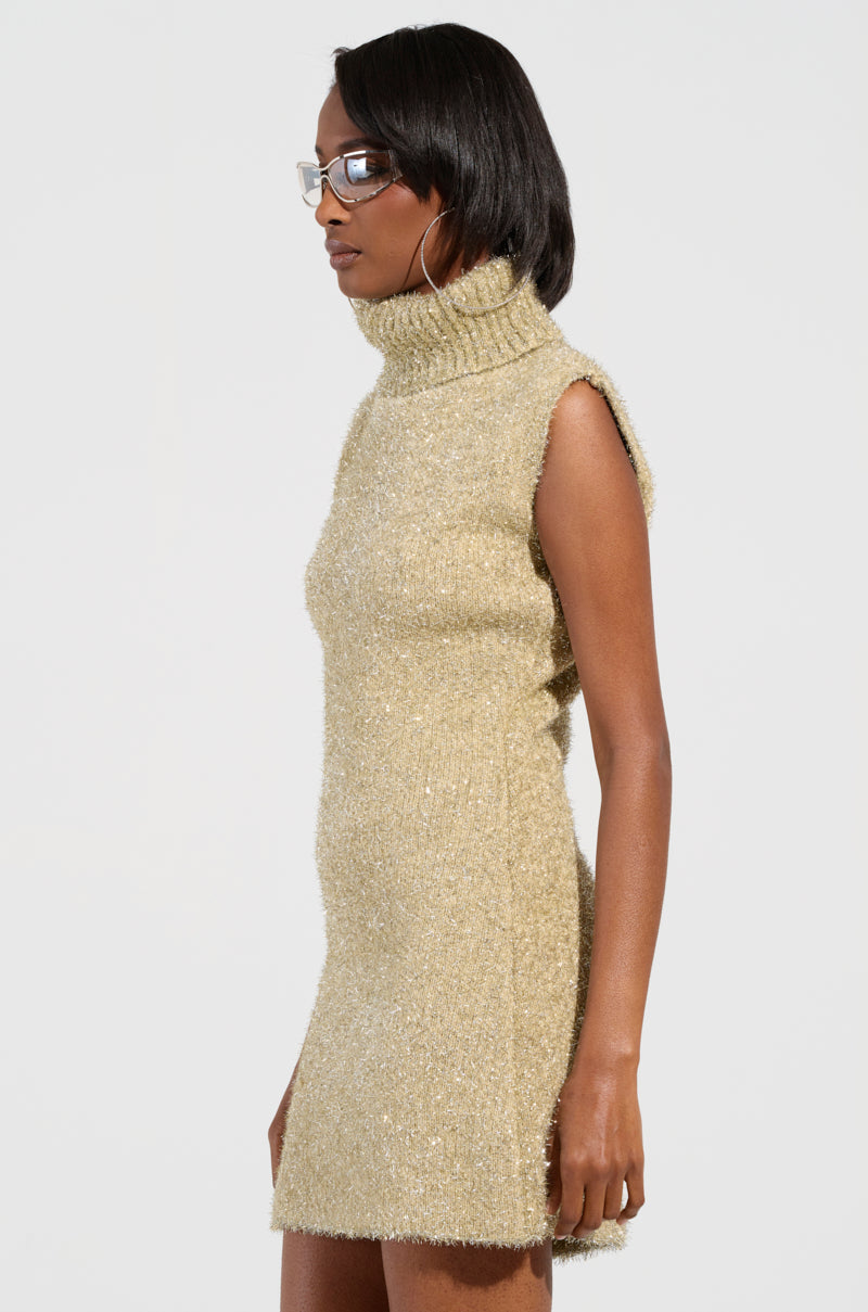 A person in the FELT A SPARK KNIT GLITTER MINI DRESS stands sideways against a plain background. They have black hair and are wearing glasses and hoop earrings, adding a chic touch to their ensemble.