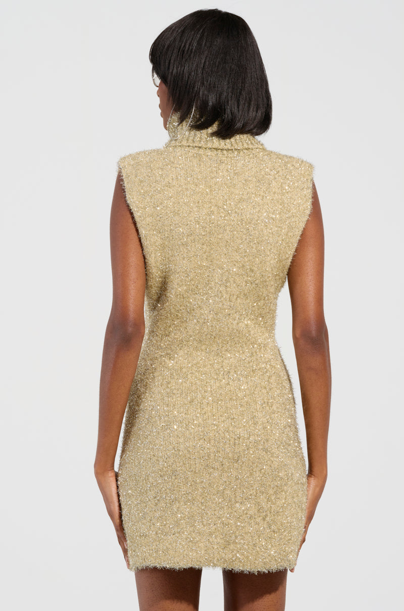Rear view of a person wearing the FELT A SPARK KNIT GLITTER MINI DRESS, which is sleeveless and features metallic gold and silver knit glitter, standing against a plain white background.