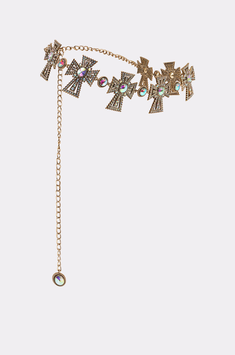 The IN ROME CHAIN BELT features gold chains adorned with ornate, gemstone-studded cross charms and a hanging chain with a circular gem, creating a bold western statement piece. 2