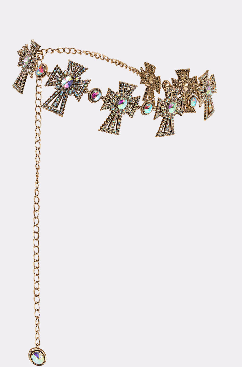 The IN ROME CHAIN BELT is a gold cross chain belt embellished with iridescent round gems and ornate crosses, featuring an adjustable dangling chain ending in a single gem, shown against a light background. 3