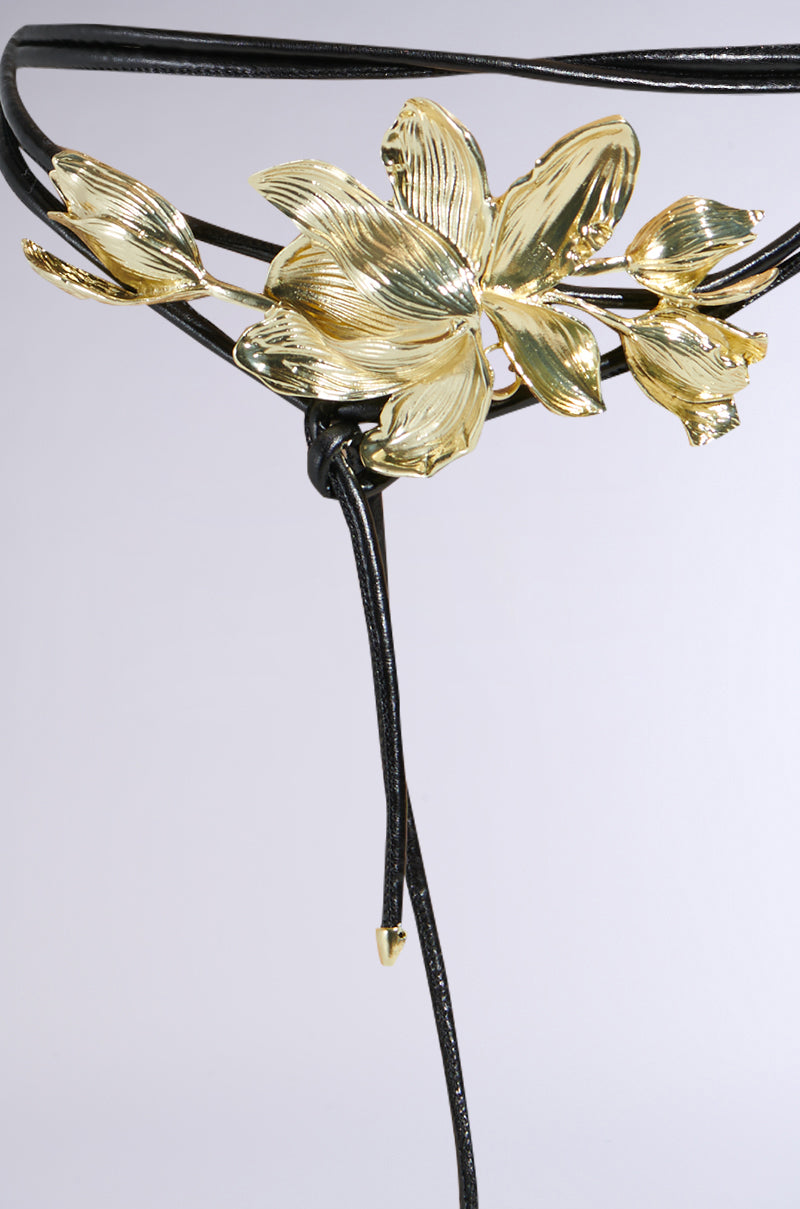 The PETAL POWER METAL DETAIL BELT is a delicate black accessory with a gold floral motif and leaf design. Thin straps enhance its statement appeal, while dangling ends tipped in gold add the perfect touch of elegance.