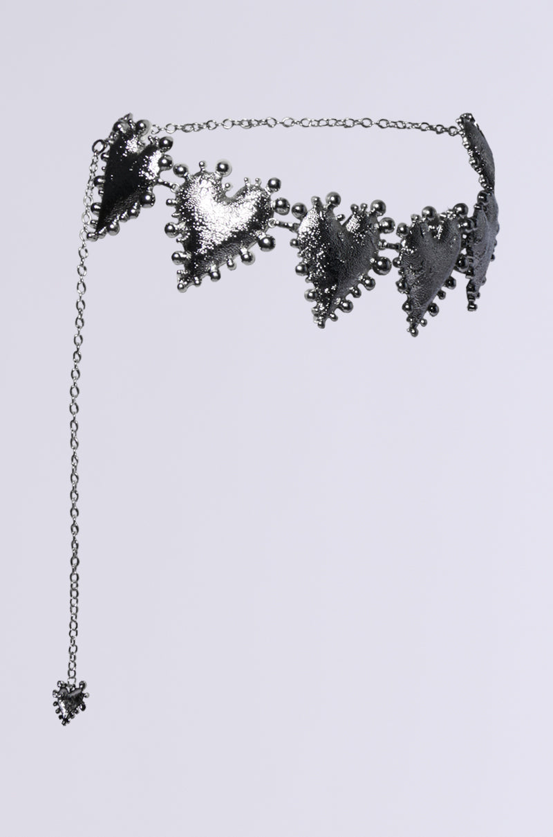 Introducing the HOLD MY HEART METAL CHAIN BELT: a silver chain belt adorned with multiple heart-shaped pendants featuring textured edges. It includes a delicate chain with an adjustable lobster clasp and showcases a single heart pendant that hangs beautifully at the end, set against a plain, light gray background.