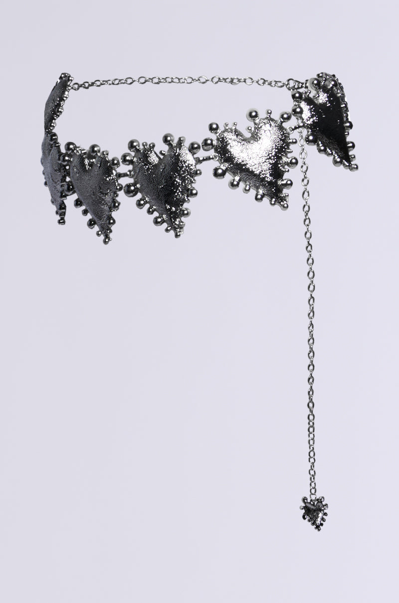 The HOLD MY HEART METAL CHAIN BELT features a silver metal chain adorned with adjustable lobster clasps. Textured heart-shaped pendants and a dangling heart charm, embellished with beaded details, add an intricate touch to its design.