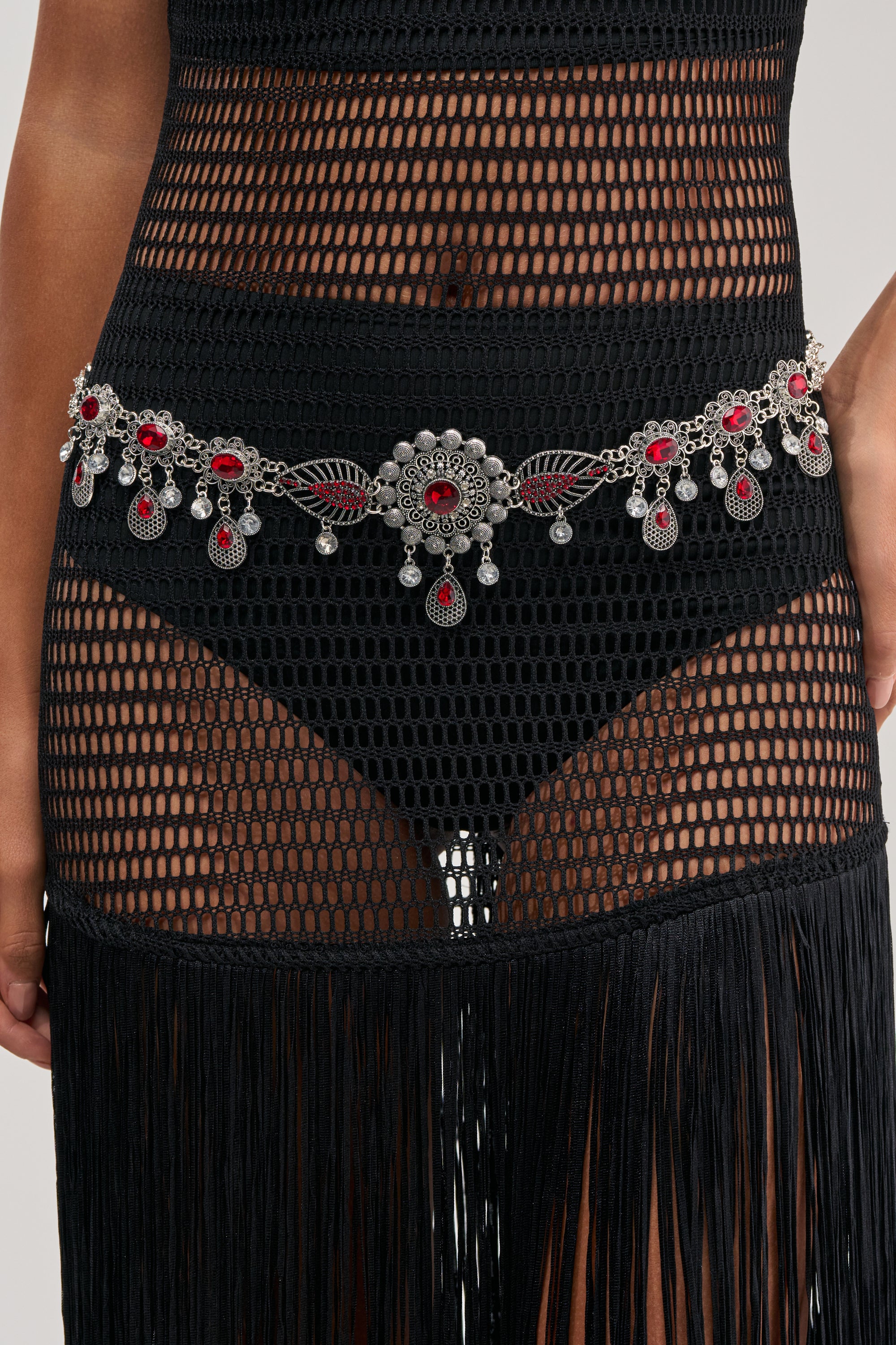 A person wears a black fishnet-style skirt with fringe, high-waisted black briefs, and the EASY LOOKING THIS GOOD CHAIN BELT—a festival-ready medallion chain belt with ruby accents and dangling decorations.