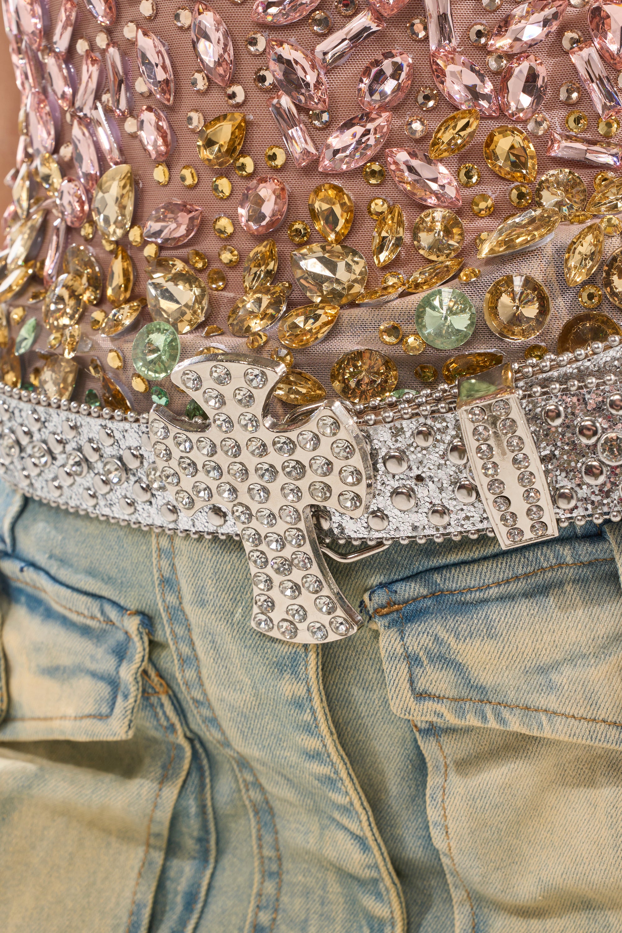 A close-up of a person wearing acid-wash jeans, a top adorned with pink, gold, and green rhinestones, and the IM BETTER BELT—a silver rhinestone belt featuring a large jeweled buckle. 3