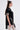 A woman in profile models the PEARL QUEEN OVERSIZED TEE, a loose black top with rhinestone trim and pearl waist chains, styled with white lace leggings, statement earrings, faux pearl brooches, and long brown hair.