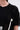 A close-up of a person wearing the PEARL QUEEN OVERSIZED TEE with black pleats, ruffled details, rhinestone trim, and a pearl chain attached to a flower brooch. Only the lower face, neck, and upper chest are shown.