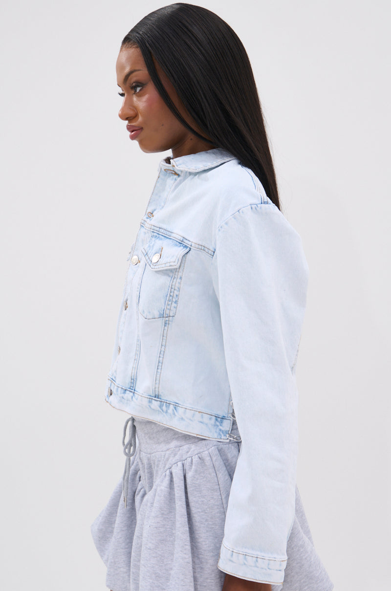 A woman with long, straight black hair is shown in profile, wearing the PARTY IN THE BACK DENIM JACKET and a gray ruffled-hem skirt, standing against a plain white background.