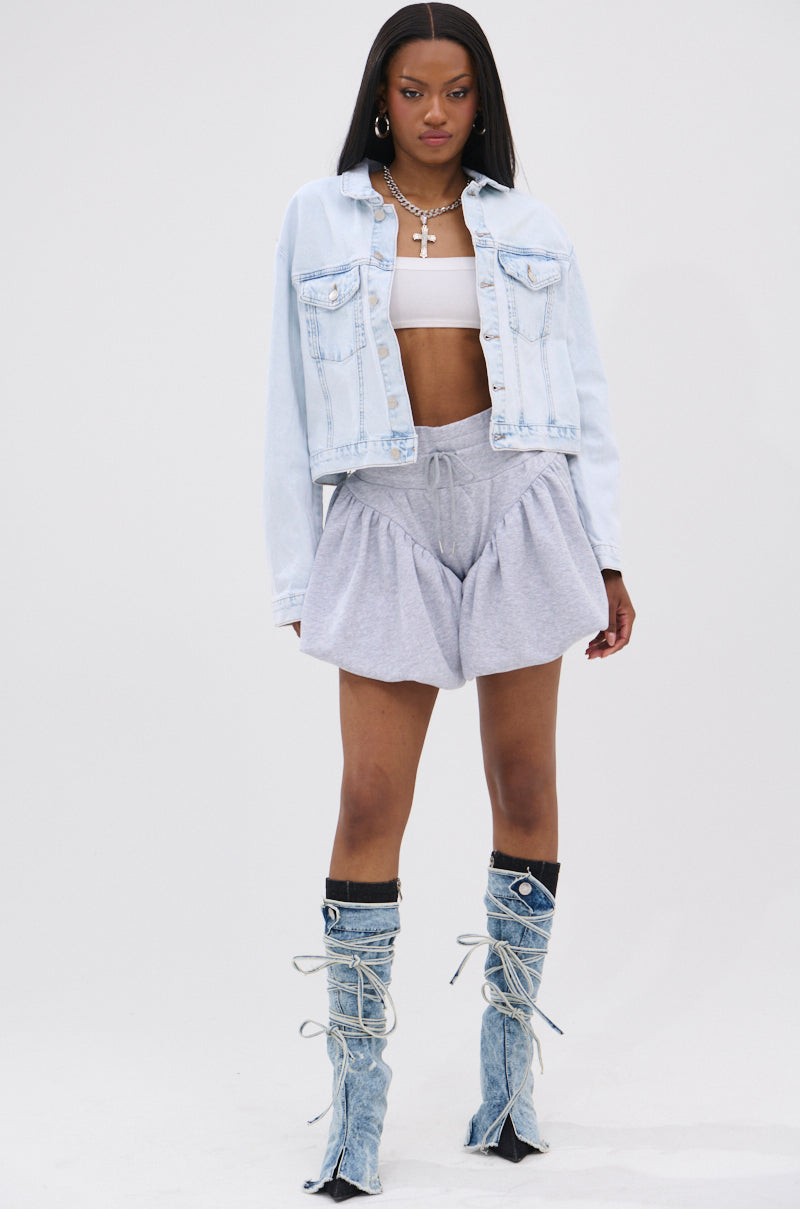 A woman faces forward wearing the PARTY IN THE BACK DENIM JACKET, a white crop top, gray drawstring shorts, knee-high lace-up denim boots, plus hoop earrings and silver-tone chain accessories.