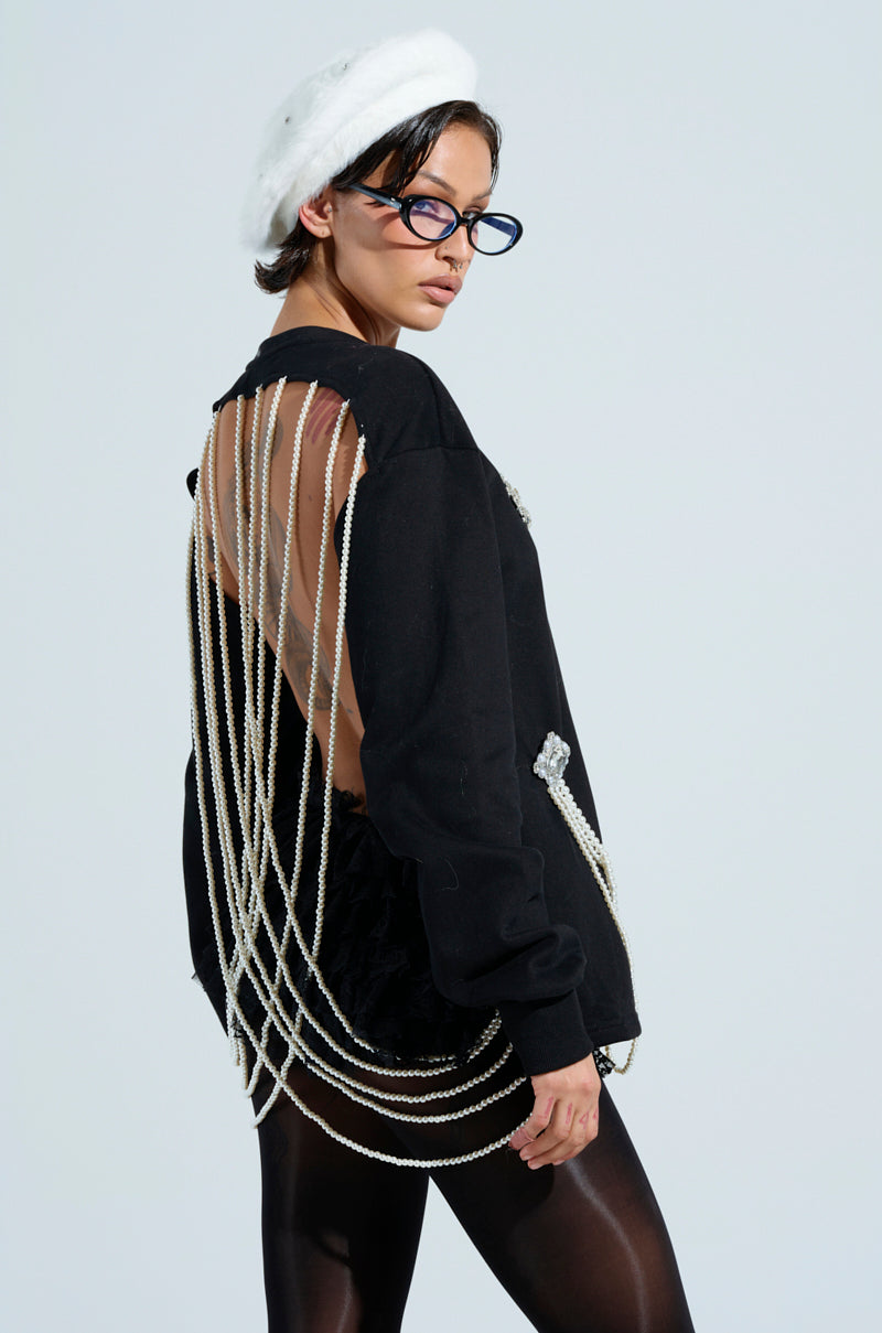 Wearing a white beret, blue glasses, and the IT'S COMPLICATED PEARL TOP with draped pearl chains on the back, this person stands out in dark tights and beaded pearl accents while posing against a plain background.