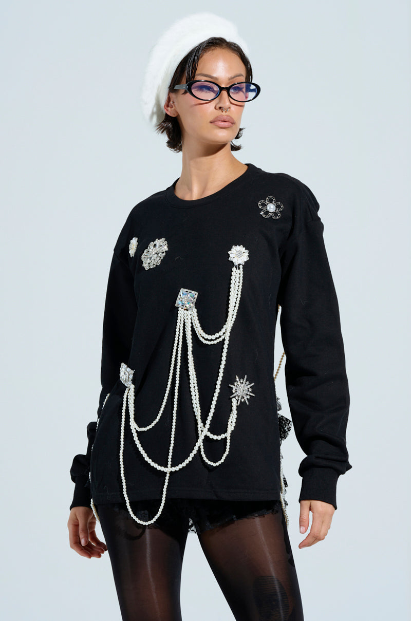 Wearing a black IT'S COMPLICATED PEARL TOP adorned with flower brooches and pearl beads, teamed with black shorts and leggings. The ensemble includes a white beret and dark glasses against a plain, light-colored background.